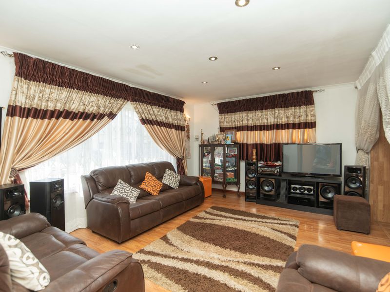 A living room featuring laminate flooring and recessed downlighting, with a visible water stain on the ceiling.