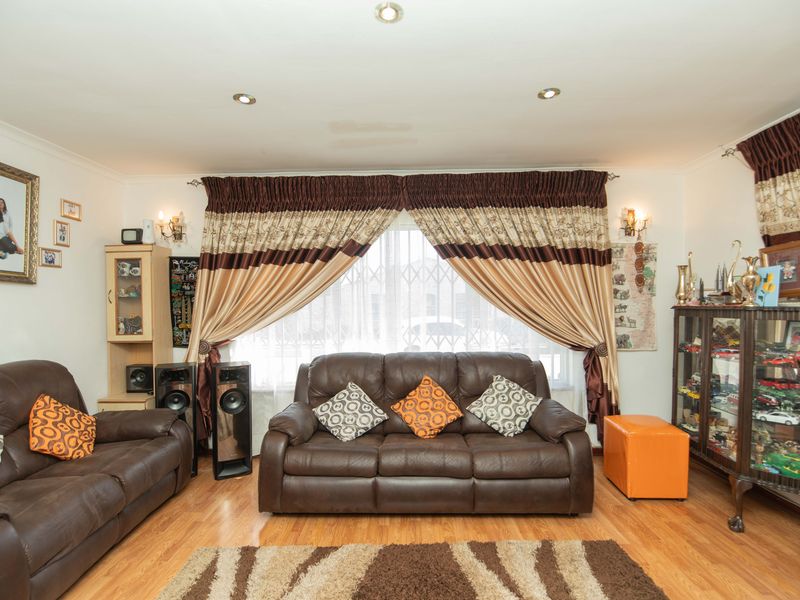 A comfortable living room featuring laminate flooring, recessed downlighting, and a large window fitted with a security gate.
