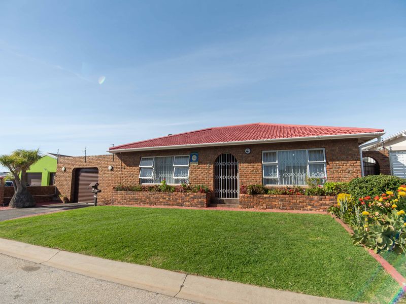 A well-maintained single-story brick home featuring a tiled roof, secure entrance gate, integrated garage, and established front garden with brick planter beds.