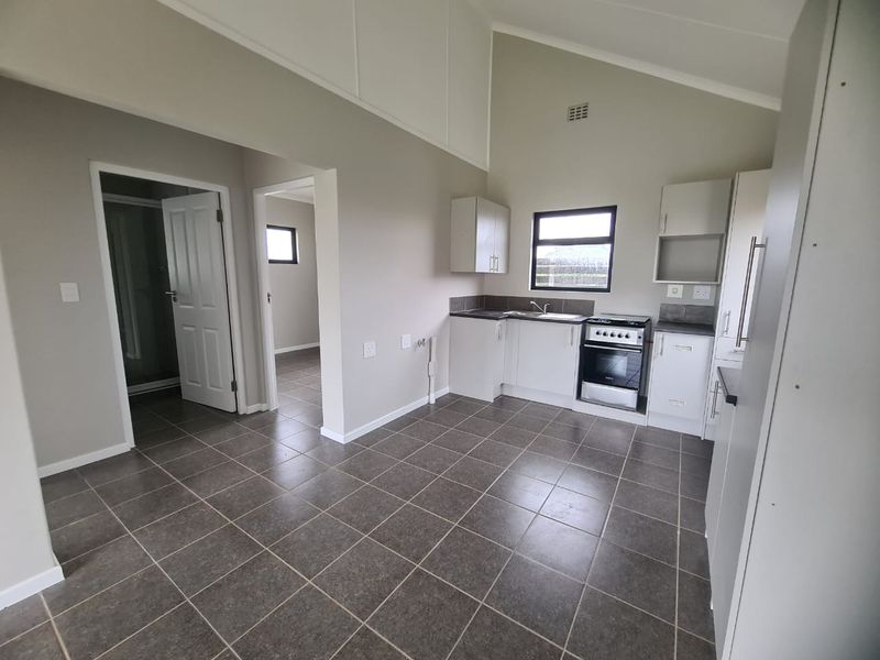 An open-plan kitchen and living area featuring tiled floors, a vaulted ceiling, and modern built-in cabinetry with a functional stove and sink.