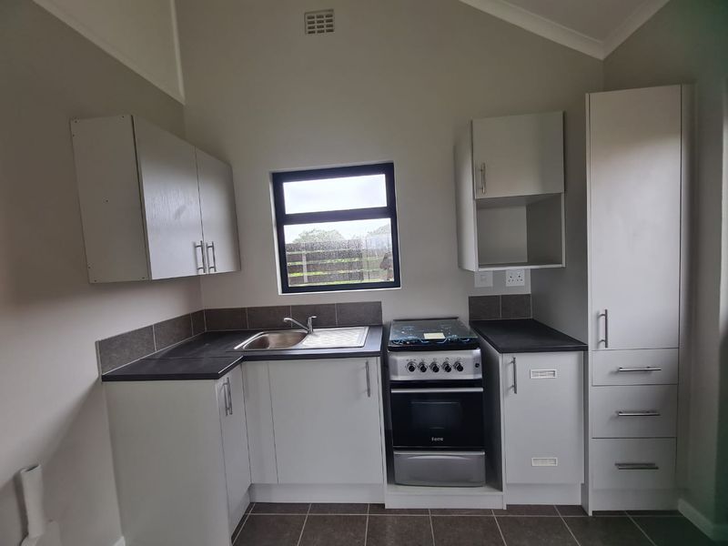 A clean and functional kitchen featuring modern cabinetry, a stainless steel sink, a freestanding stove, and tiled splashbacks with neutral finishes.