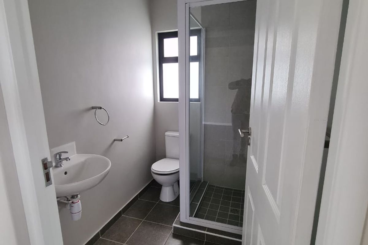 A clean and functional bathroom featuring a wall-mounted basin, a separate shower enclosure, and a toilet with neutral tiled flooring.