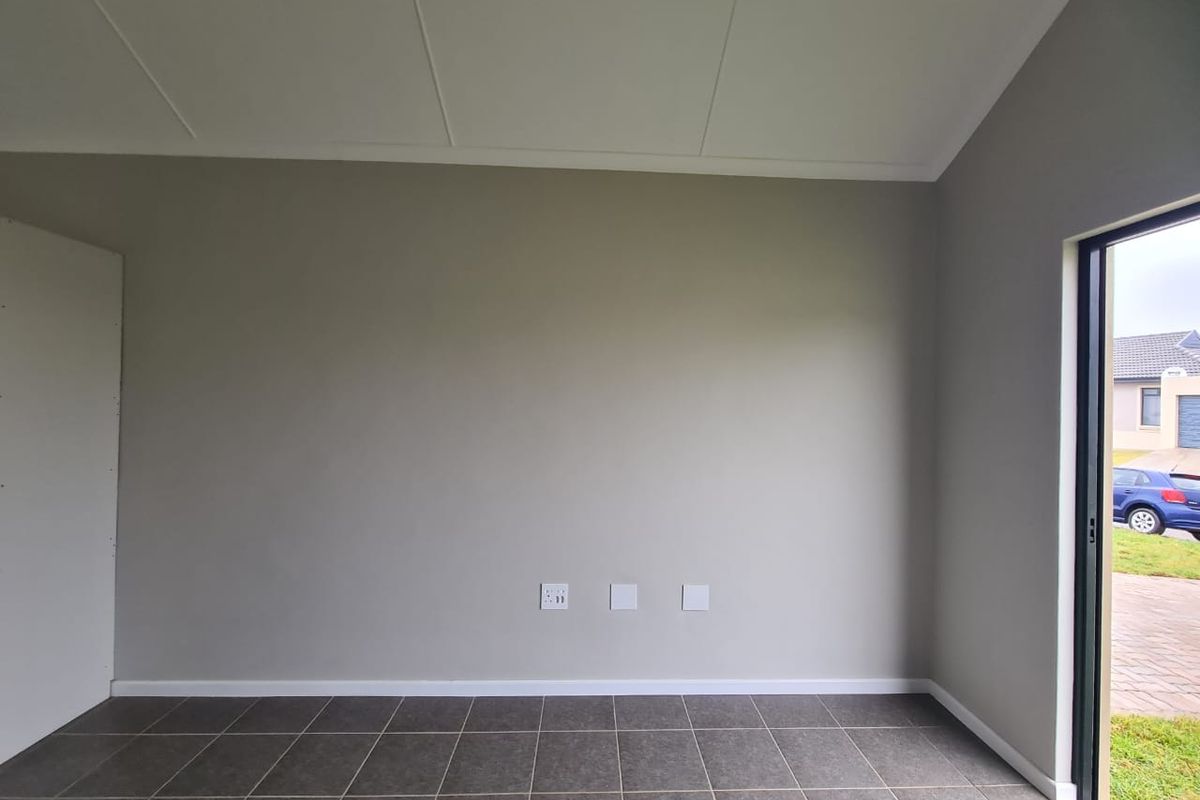 A bright, empty living area featuring neutral grey walls, dark tiled flooring, and a sliding glass door providing access to the exterior.