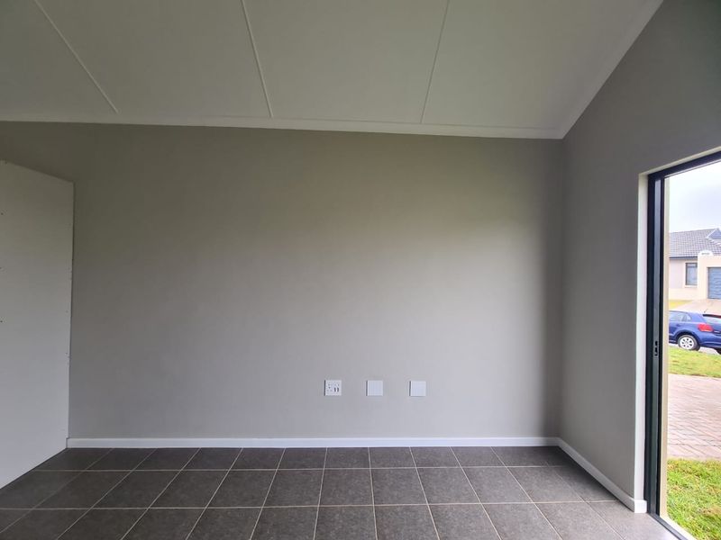 A bright, empty living area featuring neutral grey walls, dark tiled flooring, and a sliding glass door providing access to the exterior.