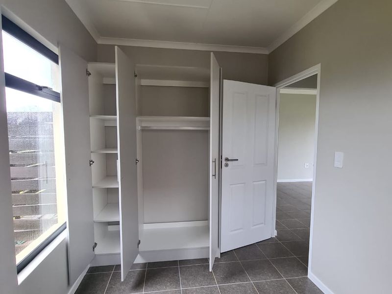 A clean, empty bedroom featuring neutral wall paint, tiled flooring, and a functional built-in wardrobe with shelving and hanging space.