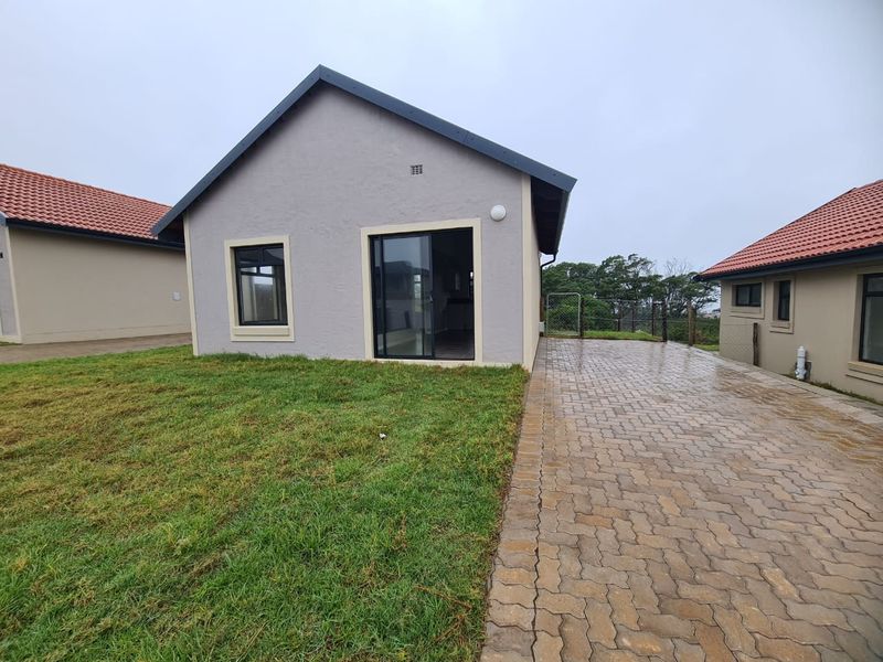 Rear view of the property featuring a paved driveway, a small lawn area, and a sliding glass door entrance.