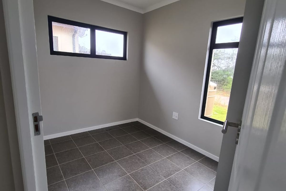 A clean, empty bedroom featuring neutral grey walls, dark tiled flooring, and modern aluminium-framed windows, providing a versatile space ready for furnishing.