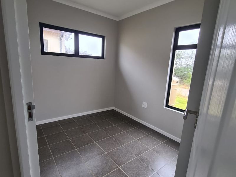 A clean, empty bedroom featuring neutral grey walls, dark tiled flooring, and modern aluminium-framed windows, providing a versatile space ready for furnishing.