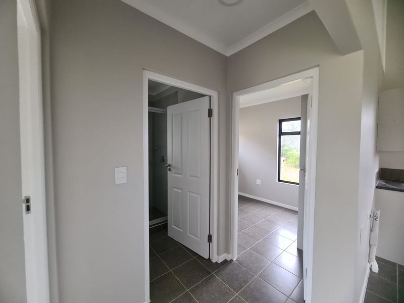 A clean, neutral-toned hallway featuring tiled flooring and access to adjacent rooms, including a bathroom and bedroom.