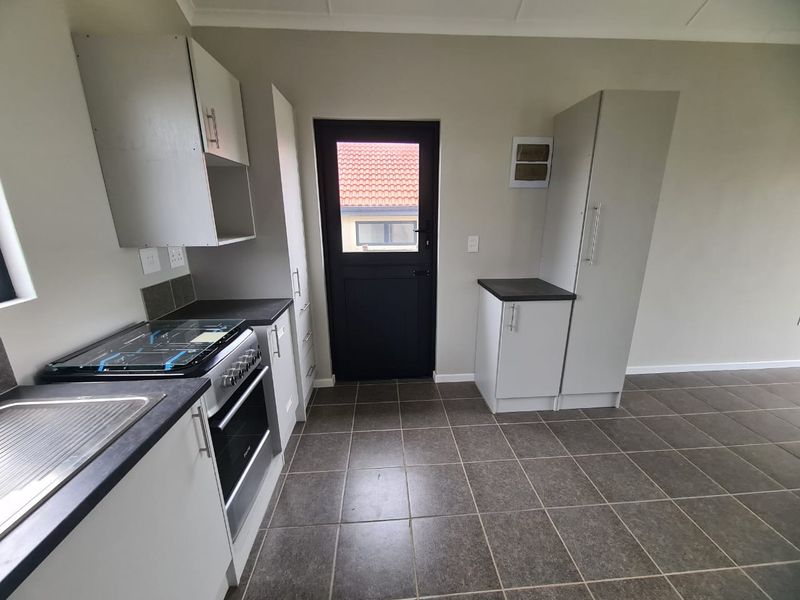 A clean, modern kitchen featuring neutral cabinetry, dark countertops, tiled flooring, and a freestanding stove, with direct access to the exterior.