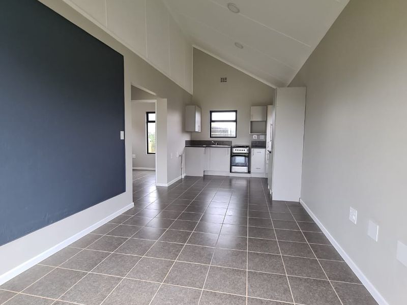 An open-plan living and kitchen area featuring vaulted ceilings, tiled flooring, and a functional kitchen layout with built-in appliances.