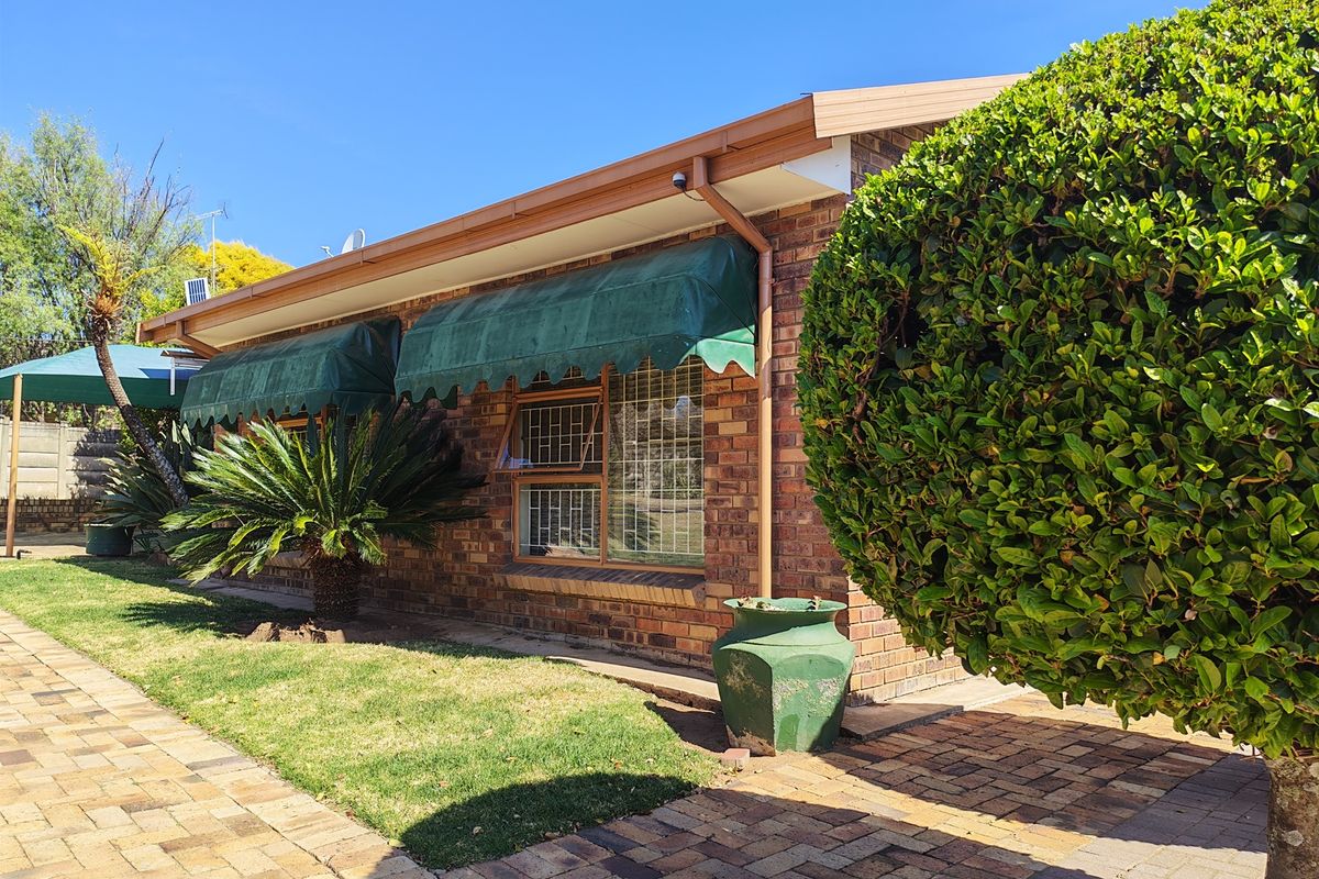 Rear exterior view of the townhouse featuring face brick walls, metal window awnings with security bars, and a paved garden walkway.