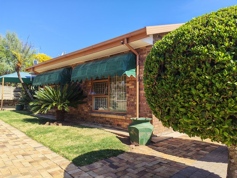 Rear exterior view of the townhouse featuring face brick walls, metal window awnings with security bars, and a paved garden walkway.