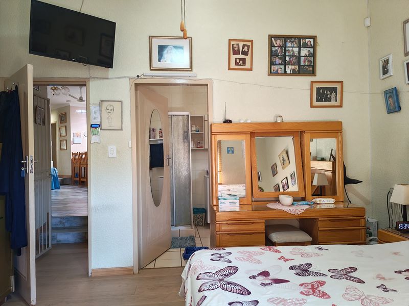 Bedroom featuring laminate flooring and an en-suite bathroom with a shower, showing signs of wear and dated finishes.