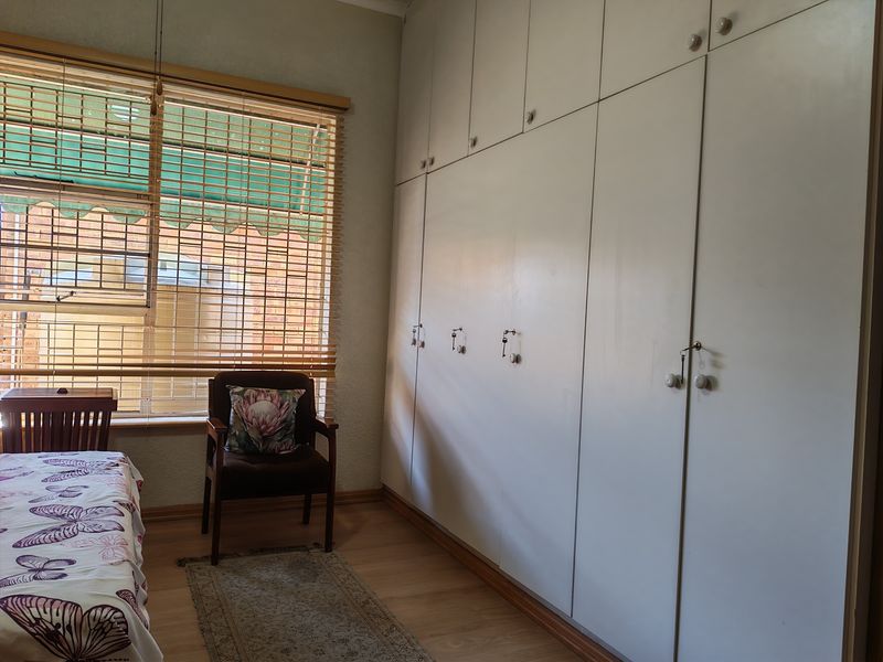 A bedroom featuring extensive floor-to-ceiling built-in cupboards, laminate flooring, and natural light filtered through wooden venetian blinds.