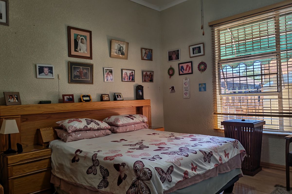 A bedroom featuring a built-in wooden headboard, laminate flooring, and natural light through venetian blinds.