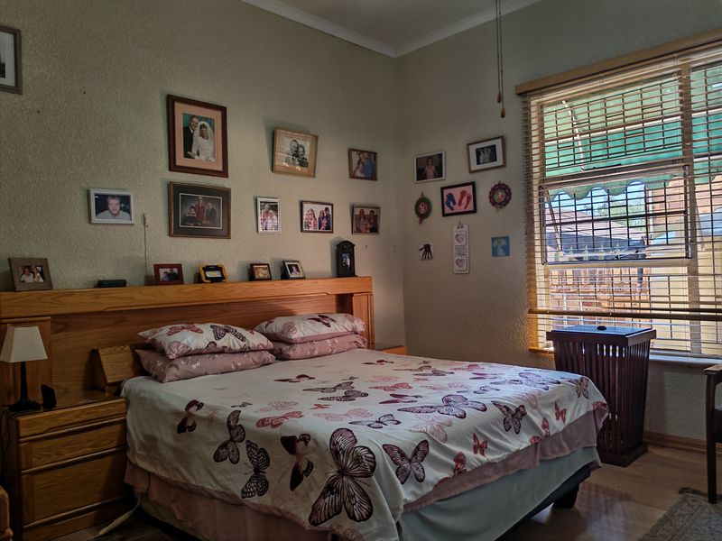A bedroom featuring a built-in wooden headboard, laminate flooring, and natural light through venetian blinds.