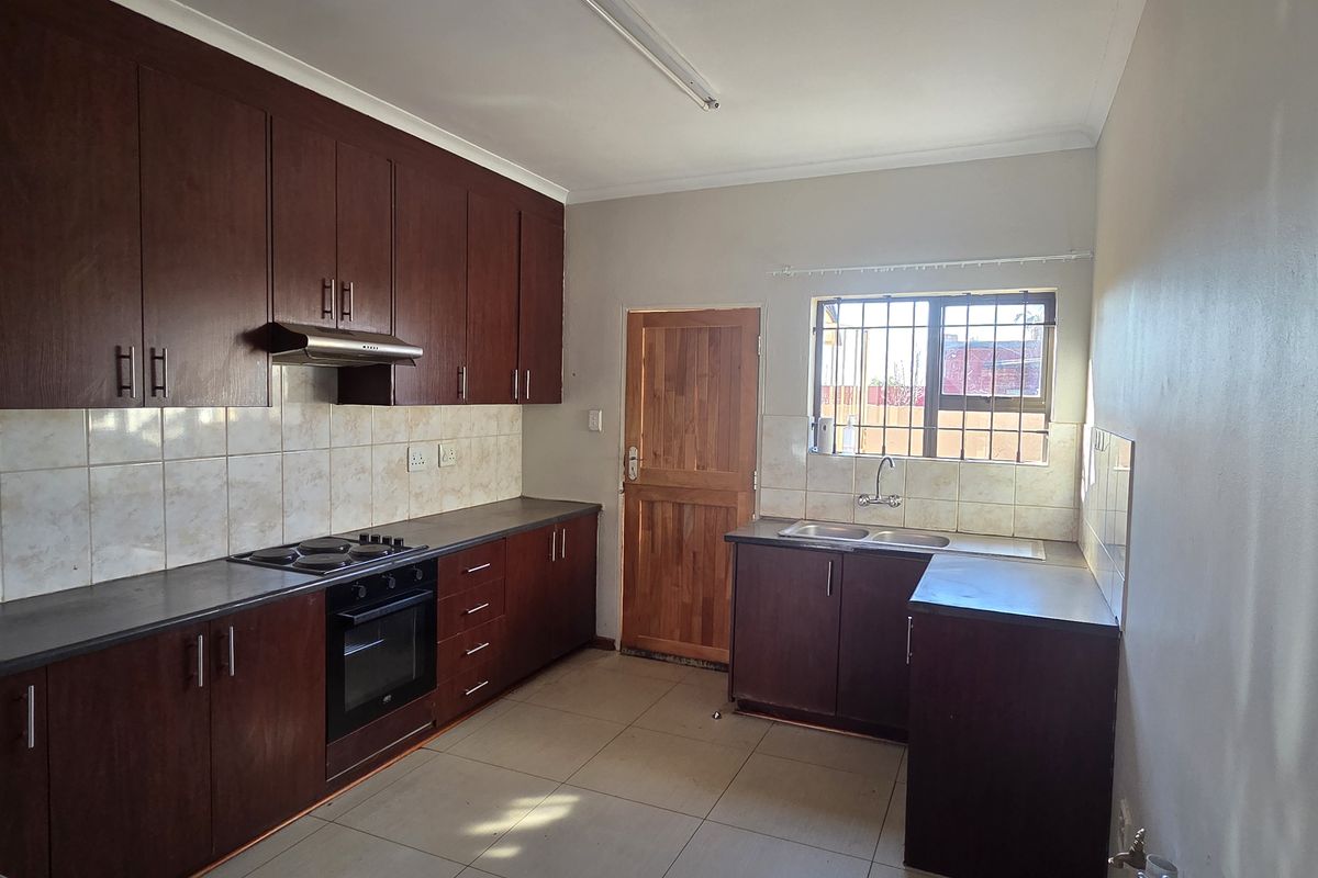 A functional kitchen featuring dark wood cabinetry, built-in oven and hob, double basin sink, and tiled flooring with a rear access door.