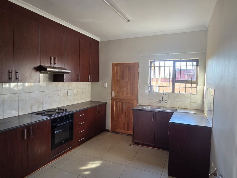 A functional kitchen featuring dark wood cabinetry, built-in oven and hob, double basin sink, and tiled flooring with a rear access door.