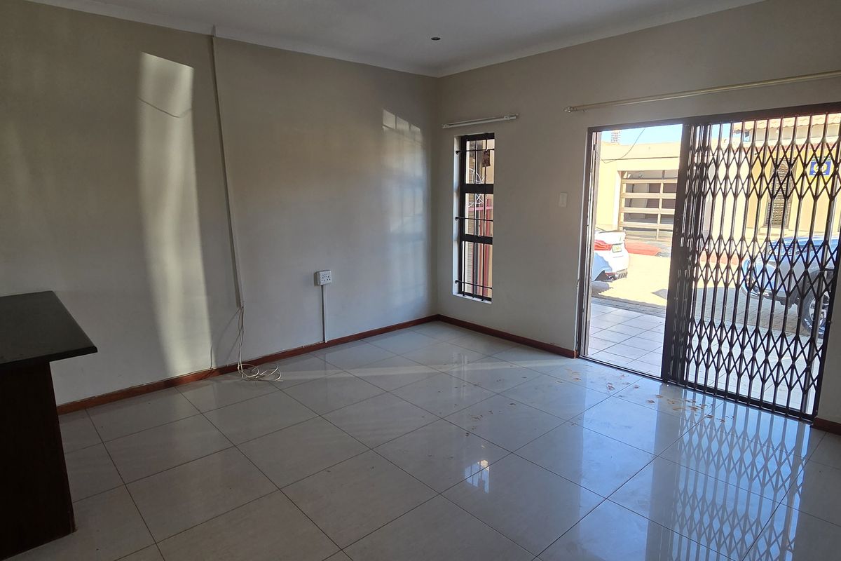 An empty living room featuring tiled flooring, a sliding glass door with a security gate, and access to the exterior.
