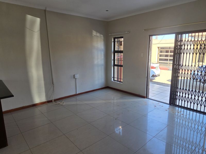 An empty living room featuring tiled flooring, a sliding glass door with a security gate, and access to the exterior.