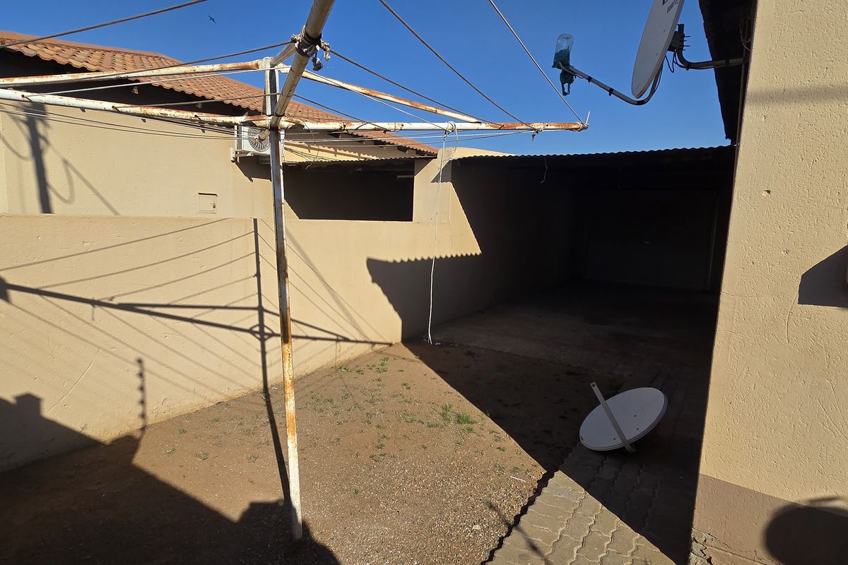 Rear exterior area of the townhouse featuring a paved section, boundary walls, and a rotary clothesline, with access to a covered parking space.