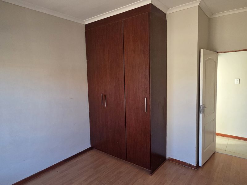 A clean, empty bedroom featuring laminate flooring and a built-in wooden wardrobe, offering a neutral canvas for personalization.