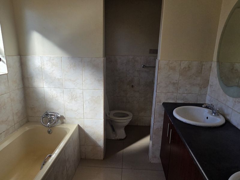 A functional bathroom featuring a bathtub, double vanity with basin, and a separate toilet area with neutral wall tiling.