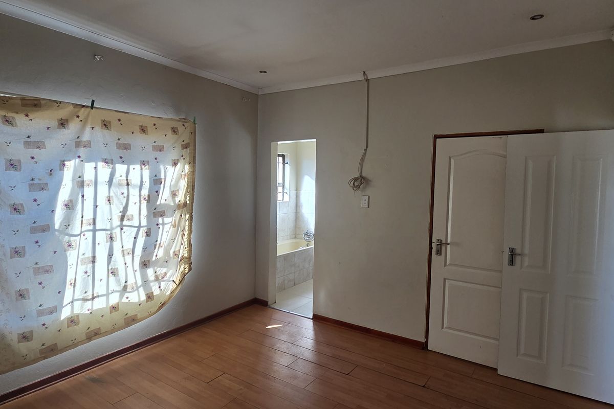 An empty bedroom featuring laminate flooring, recessed lighting, and an en-suite bathroom access point, requiring minor cosmetic repairs to wall finishes.