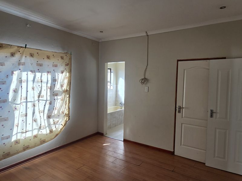 An empty bedroom featuring laminate flooring, recessed lighting, and an en-suite bathroom access point, requiring minor cosmetic repairs to wall finishes.
