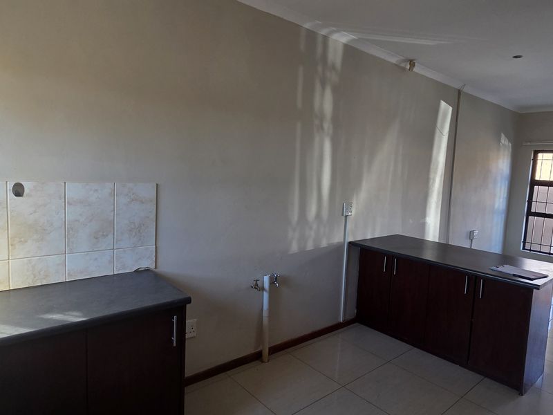 A functional, empty kitchen area featuring dark wood-look cabinetry, laminate countertops, a stainless steel sink, and tiled splashbacks with neutral floor tiles.