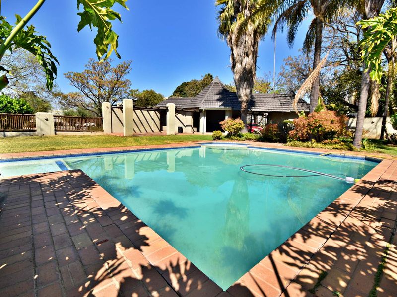 Outdoor pool area featuring a swimming pool with brick paving and a surrounding garden with mature trees.