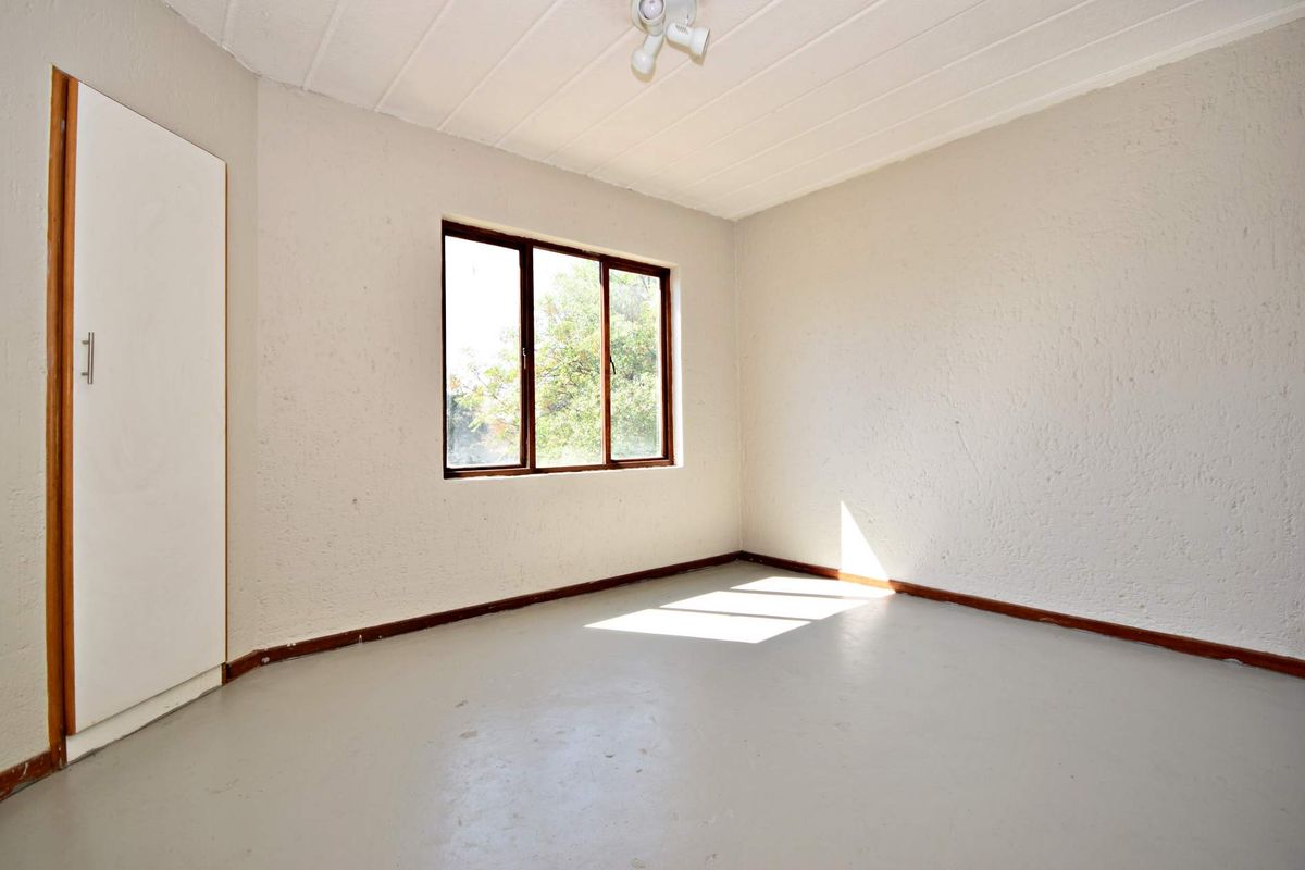 A vacant bedroom featuring a built-in cupboard, timber-framed window, and painted concrete flooring, offering a blank canvas for personalization.