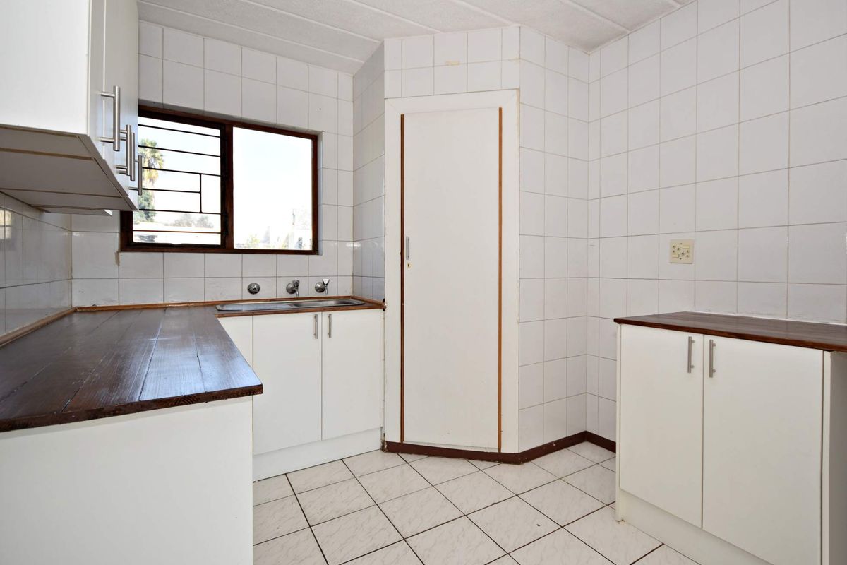A functional kitchen featuring white cabinetry, dark laminate countertops, tiled walls and flooring, and a window with security bars.
