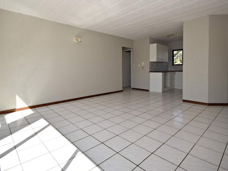 An empty open-plan living and kitchen area featuring tiled flooring, neutral walls, and basic built-in kitchen cabinetry.