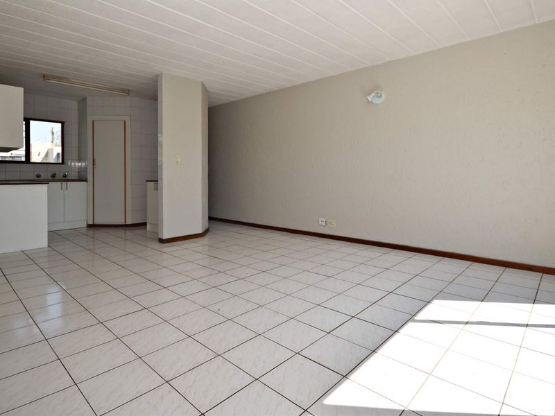 An open-plan living and kitchen area featuring tiled flooring, neutral walls, and functional kitchen cabinetry in a clean, vacant space.