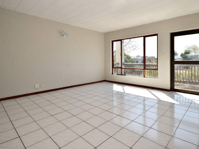 A bright, empty living room featuring white tiled flooring, textured walls, and direct access to an outdoor balcony area.