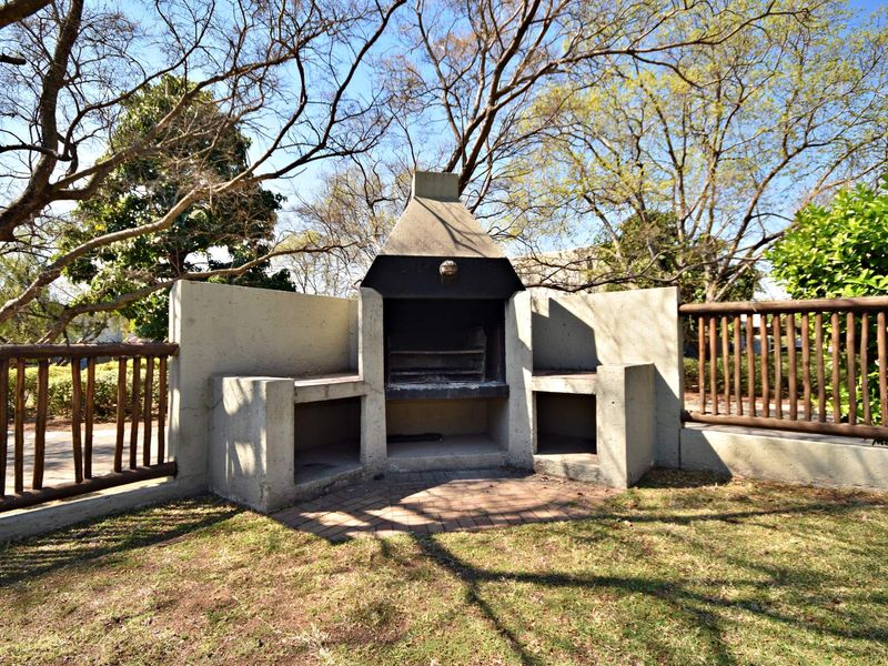 Outdoor garden area featuring a built-in concrete braai, brick paved base, and timber fencing, set within a landscaped communal space.