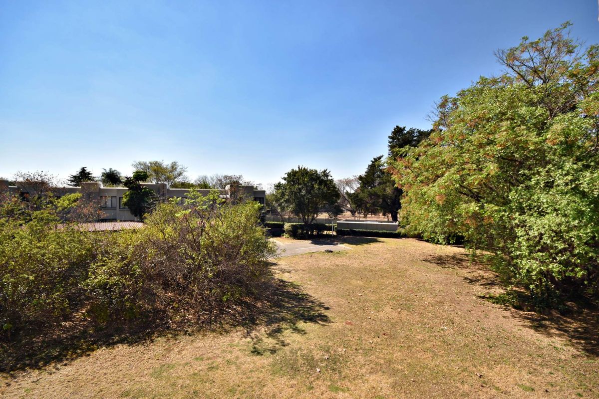 A view of the rear garden area featuring established trees and a paved driveway section within the apartment complex grounds.