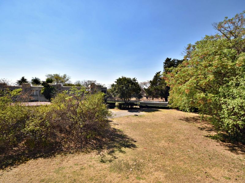 A view of the rear garden area featuring established trees and a paved driveway section within the apartment complex grounds.