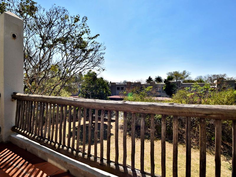 A balcony featuring a rustic wooden balustrade, tiled flooring, and views over the surrounding garden and neighborhood.