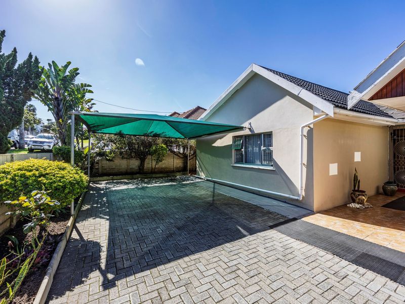 Front exterior view featuring a paved driveway with a shade sail carport, tiled entrance area, and established garden boundary wall.