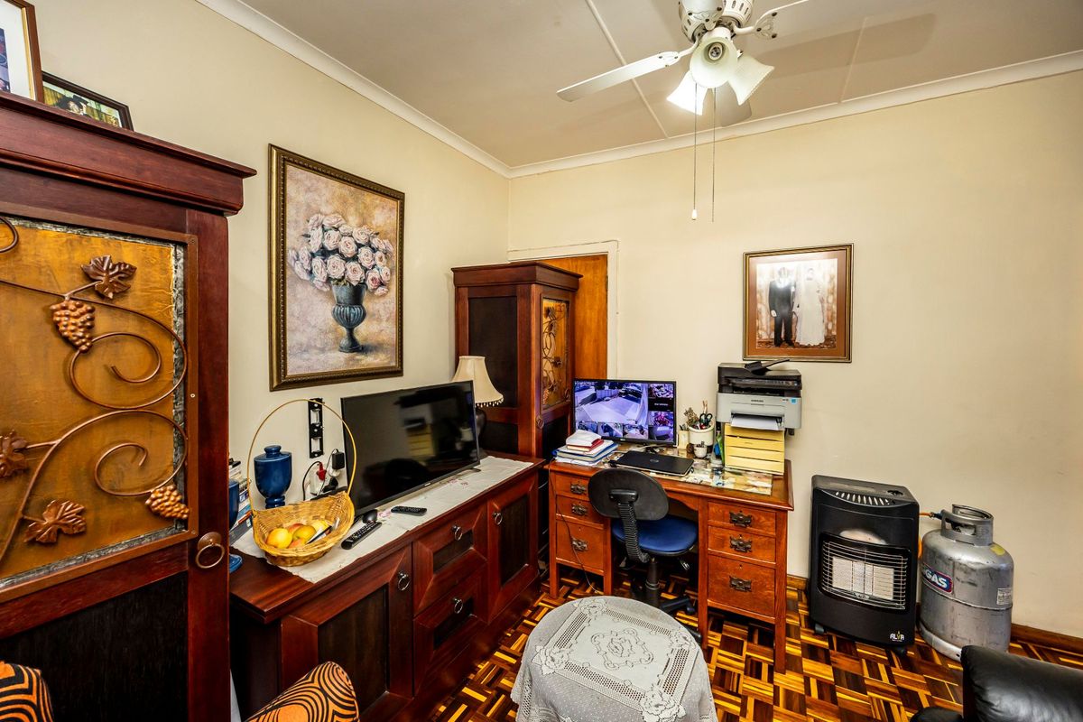A bedroom featuring parquet flooring, coved cornicing, and a ceiling fan, currently utilized as a home office and storage space.