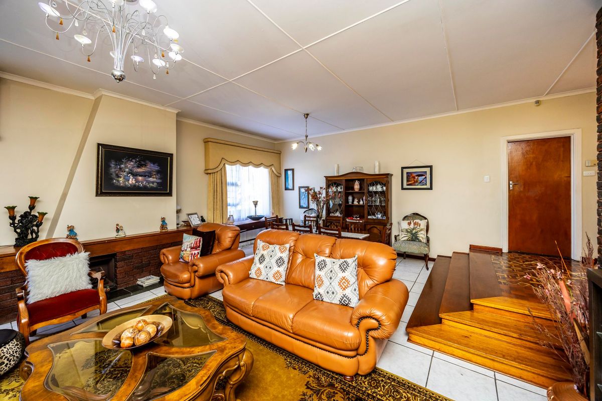 Spacious living room featuring a brick fireplace, tiled and parquet flooring, and a raised wooden staircase leading to an adjacent area.