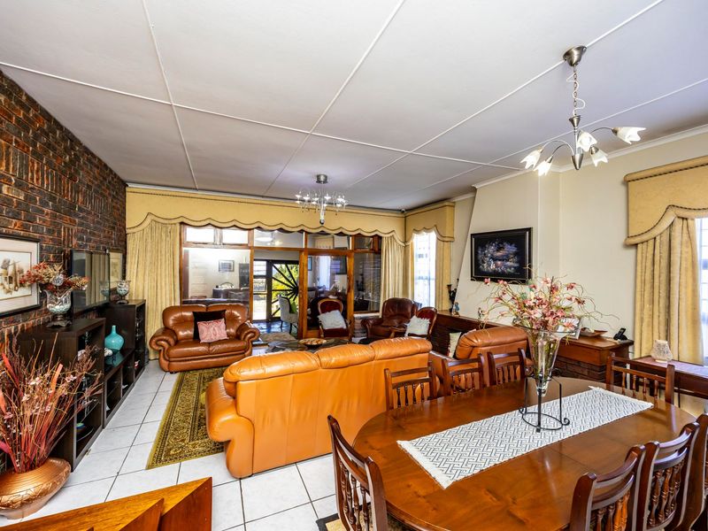 Spacious open-plan living and dining area featuring an exposed brick feature wall, tiled flooring, and direct access to an enclosed patio through sliding glass doors.