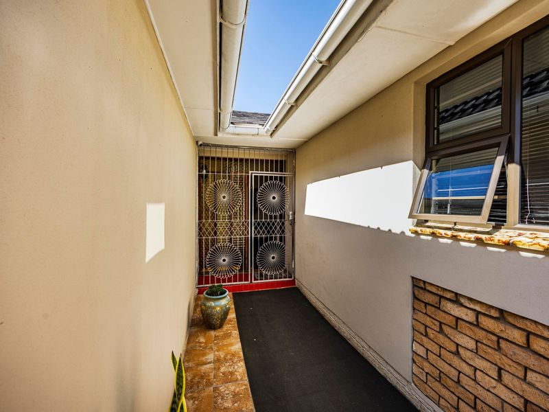 A narrow exterior side passage featuring tiled flooring, a security gate, and brick accents, providing access to the rear of the property.