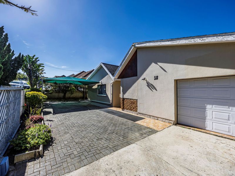 Front exterior view of the property featuring a paved driveway, single garage, and a shaded parking area with perimeter security fencing.