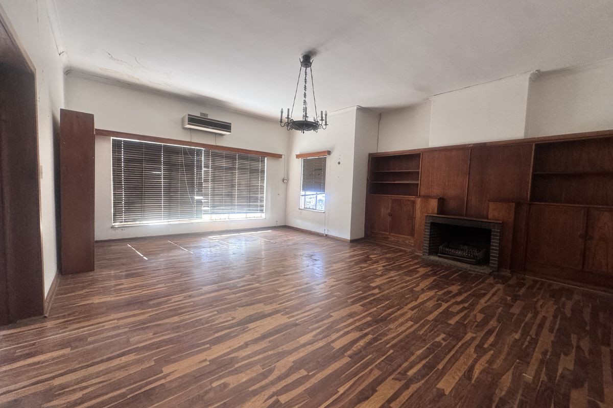 Spacious living room featuring original wooden flooring, built-in cabinetry, and a fireplace, offering a blank canvas for renovation and modernization.