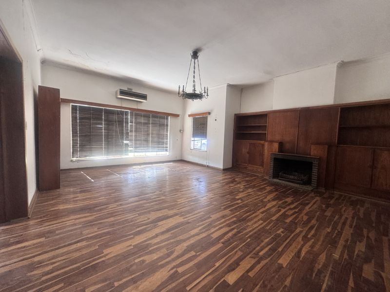 Spacious living room featuring original wooden flooring, built-in cabinetry, and a fireplace, offering a blank canvas for renovation and modernization.