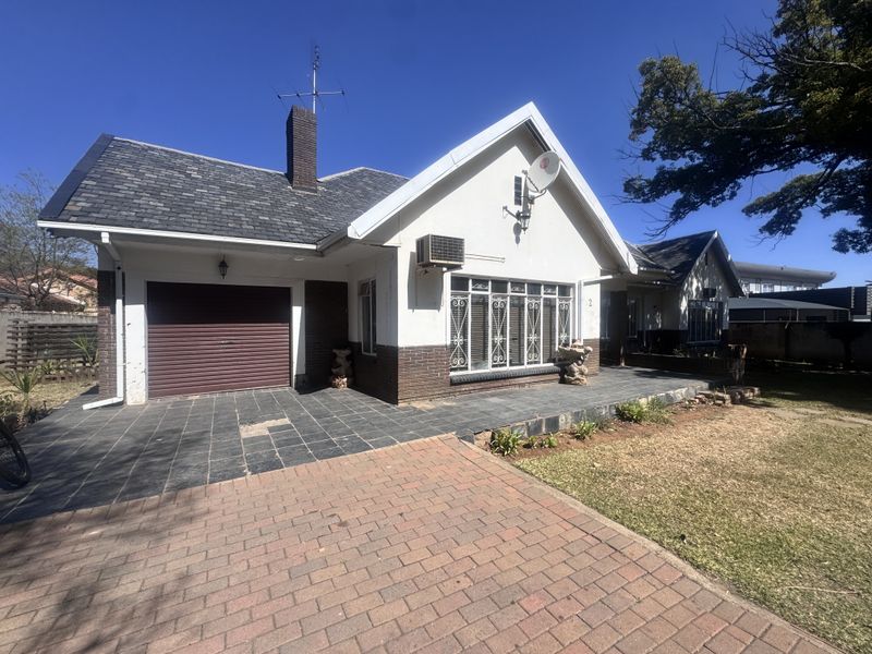 Front elevation of a single-story house featuring a tiled roof, brick chimney, paved driveway, and an integrated garage with a roller door.